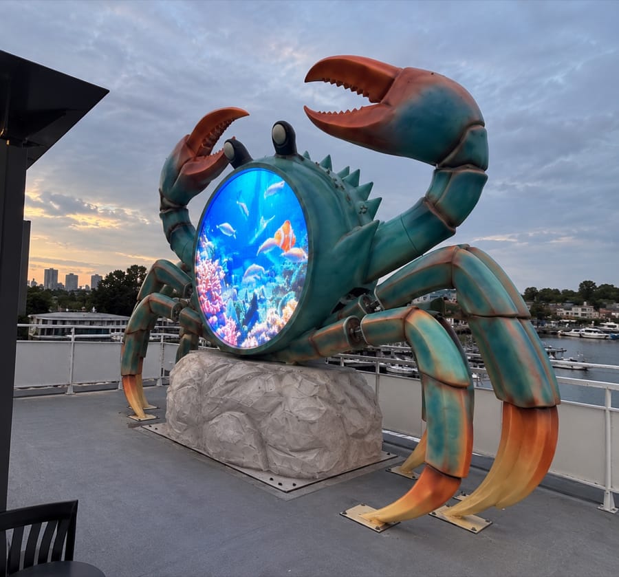 The same circular LED crab installation photographed from the side at dusk