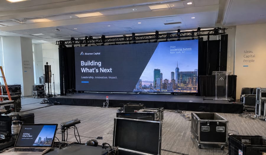 LED wall on truss behind a corporate keynote stage, screen showing a leadership summit title slide